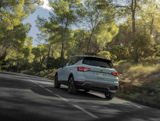 De lichtblauwe Seat Arona crossover rijdt dynamisch over een kronkelende weg in het bos.