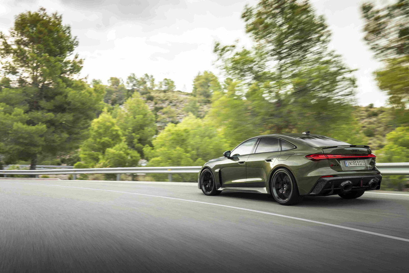 Een donkergroene Audi RS5 Berline die dynamisch door een bochtige bergweg rijdt.
