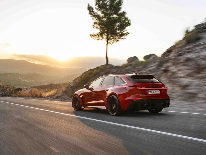 Rode Audi RS5 Avant rijdt dynamisch op bergweg tijdens zonsondergang, met sportieve velgen.