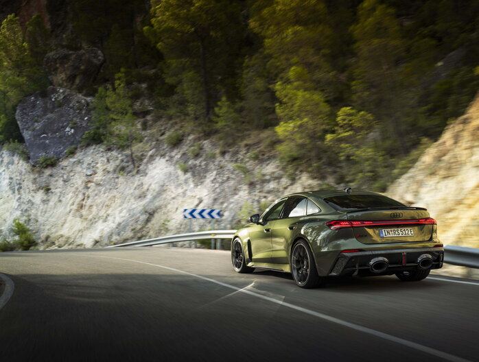 Een donkergroene Audi RS5 Berline die sportief door een scherpe bocht navigeert op een bergachtige weg.
