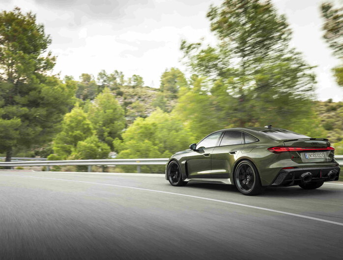 Een donkergroene Audi RS5 Berline die dynamisch door een bochtige bergweg rijdt.