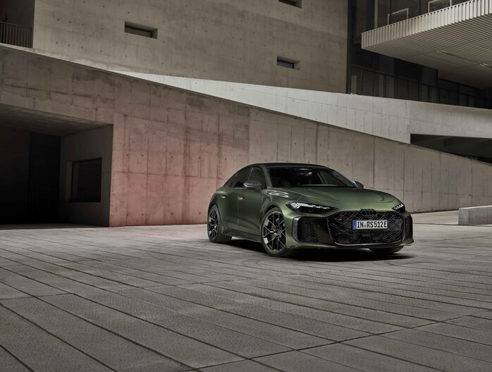 Audi RS5 Sportback in donkergroene lak geparkeerd voor moderne betonnen architectuur met sportieve velgen en agressieve RS styling