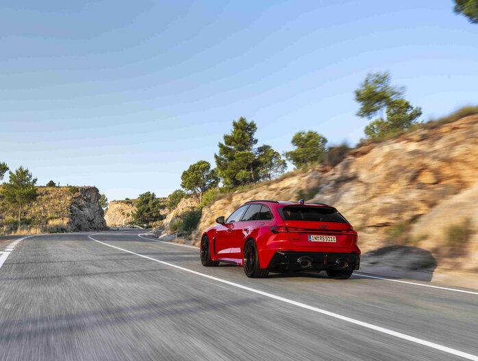 Rode Audi RS5 rijdt dynamisch over bochtige bergweg, met sportieve zwarte velgen.