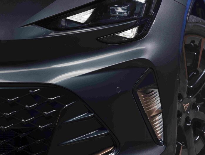 De donkergrijze Cupra Born toont zijn opvallende LED koplampen en stijlvolle koperen details.