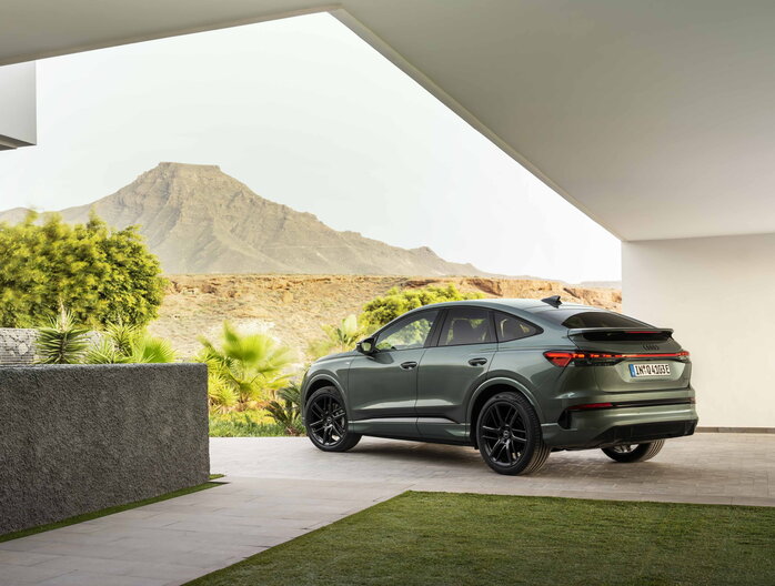 Donkergroene Audi Q4 SUV met glanzende zwarte velgen geparkeerd voor een berg.