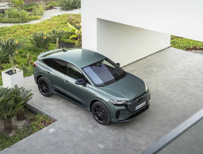 Donkergroene Audi Q4 e-tron Sportback SUV met zwarte velgen geparkeerd in moderne tuin.