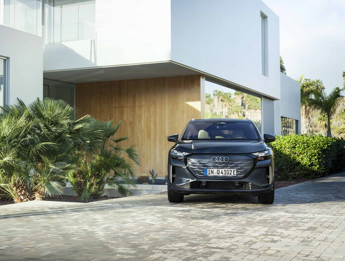 Donkergrijze Audi Q4 e-tron SUV met prominent logo geparkeerd voor een moderne woning.