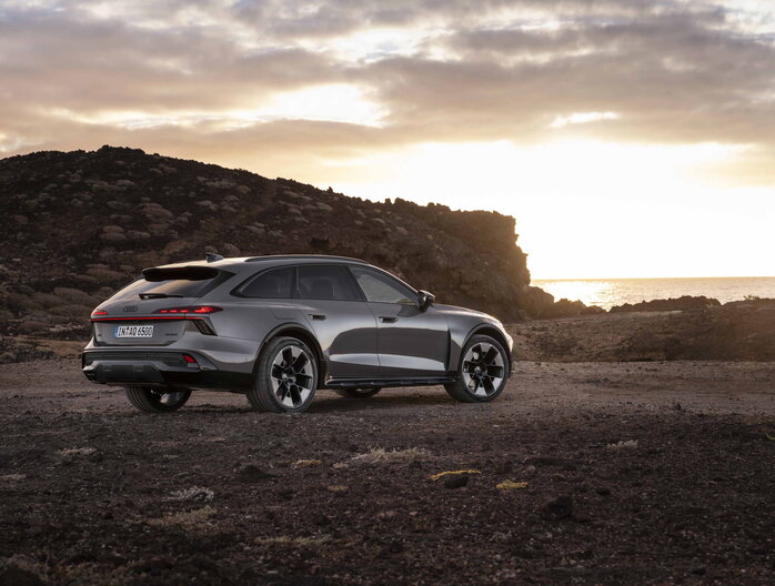 Dynamische achterkant van de donkergrijze Audi A6 Allroad in avondlicht bij rotsachtig landschap.