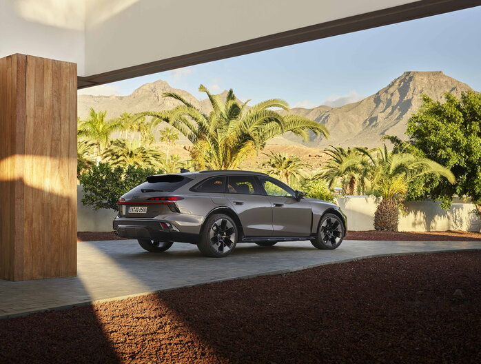 Grijze Audi A6 Allroad geparkeerd bij luxe villa met palmbomen en bergen.