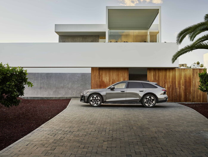 Grijze Audi A6 Allroad geparkeerd op oprit voor moderne architectuur.