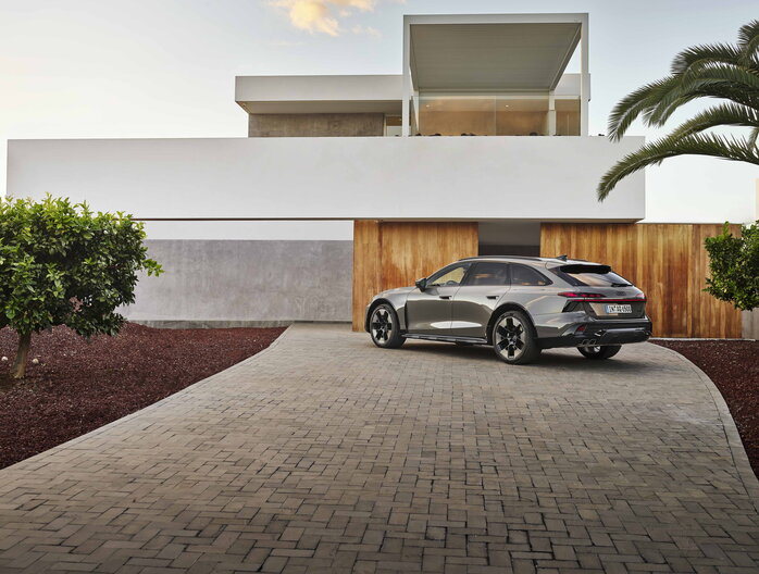 Grijze Audi A6 Allroad geparkeerd bij moderne villa, stijlvolle achterzijde.