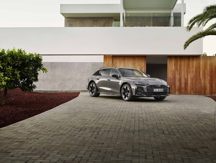 Grijze Audi A6 Allroad geparkeerd bij moderne villa, krachtige voorzijde.