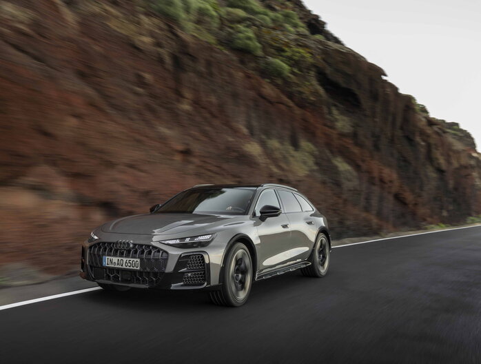 Grijze Audi A6 Allroad sportief rijdend op bochtige weg langs rotsachtige kliffen.