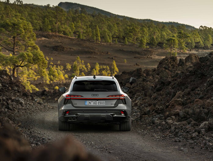 Grijze Audi A6 Allroad van achteren op onverharde weg door vulkanisch landschap.