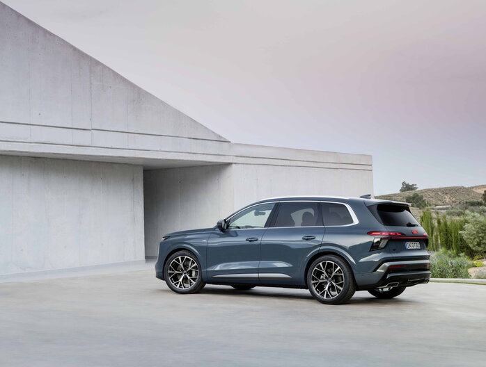 Petrolblauwe Audi Q7 SUV, achterkant en zijkant, met strak design tegen moderne architectuur.