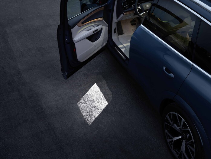 Audi Q7 met geopende deur, toont interieur en een lichtprojectie op de grond.