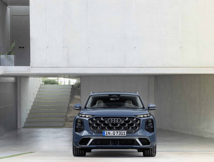 Audi Q7 SUV in petrolblauw, vooraanzicht, met prominente grille onder betonnen overhang.