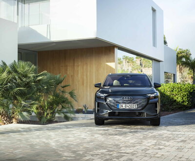 Donkergrijze Audi Q4 e-tron SUV met prominent logo geparkeerd voor een moderne woning.