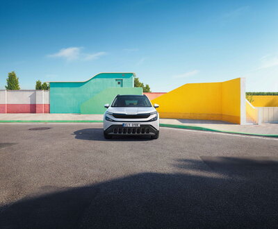 Witte Škoda Epiq elektrische SUV staat geparkeerd, vooraanzicht, voor moderne kleurrijke gebouwen.