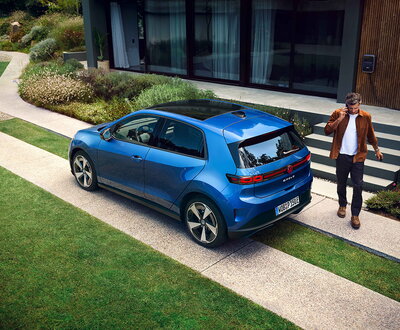 Blauwe Volkswagen Id.Polo elektrisch geparkeerd voor modern huis met man.