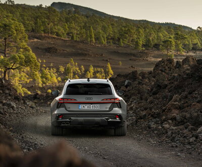 Grijze Audi A6 Allroad van achteren op onverharde weg door vulkanisch landschap.
