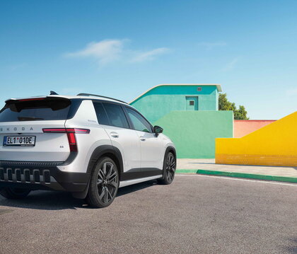 Witte Škoda Epiq compacte SUV, achterzijde zijaanzicht, geparkeerd op kleurrijke locatie.