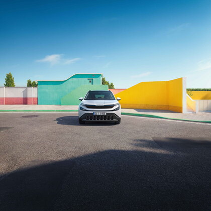 Witte Škoda Epiq elektrische SUV staat geparkeerd, vooraanzicht, voor moderne kleurrijke gebouwen.