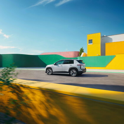 Witte Škoda Epiq elektrische SUV rijdt dynamisch langs felgekleurde muren onder blauwe lucht.