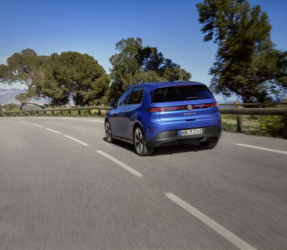 Blauwe Volkswagen ID.Polo rijdt op een kronkelende weg met bomen.