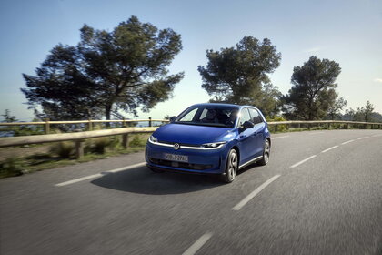 Blauwe Volkswagen Id.Polo rijdt dynamisch over een kronkelende weg met bomen en een blauwe lucht.
