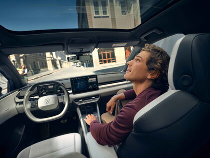 Interieur van de blauwe Volkswagen ID.Polo met man genietend van panoramadak.