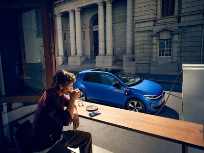 Blauwe Volkswagen ID.Polo laadt op straat terwijl man koffie drinkt.