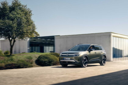 Groene Volkswagen ID. Cross rijdt dynamisch op een zonnige weg voor moderne gebouwen.