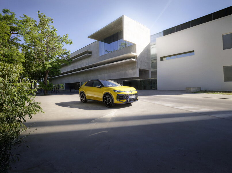 Gele Volkswagen T-Roc geparkeerd voor een modern gebouw in de zon