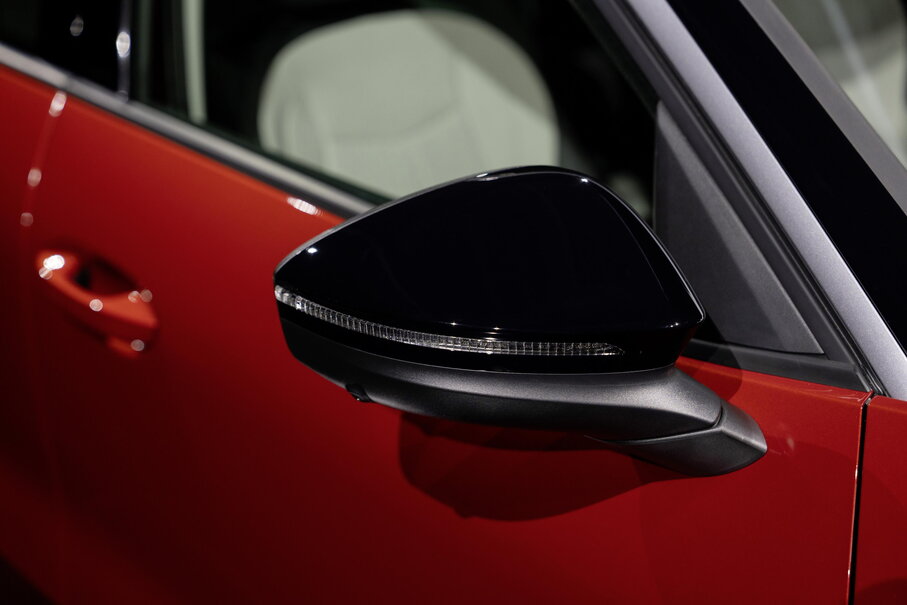 Zwarte buitenspiegel van de rode Volkswagen T-Roc met geïntegreerde richtingaanwijzer.