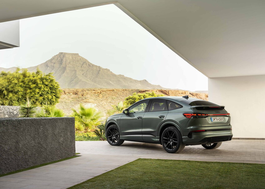 Donkergroene Audi Q4 SUV met glanzende zwarte velgen geparkeerd voor een berg.