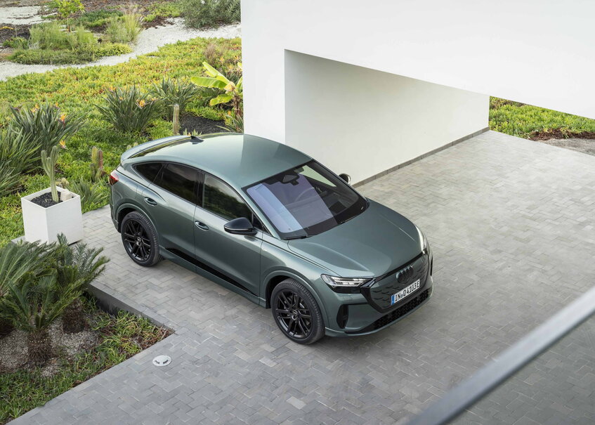 Donkergroene Audi Q4 e-tron Sportback SUV met zwarte velgen geparkeerd in moderne tuin.