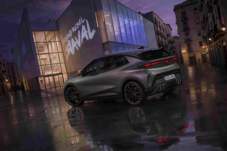Donkergrijze Cupra Raval elektrische auto met koperkleurige velgaccenten op natte straat in de nacht.