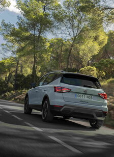 De lichtblauwe Seat Arona crossover rijdt dynamisch over een kronkelende weg in het bos.