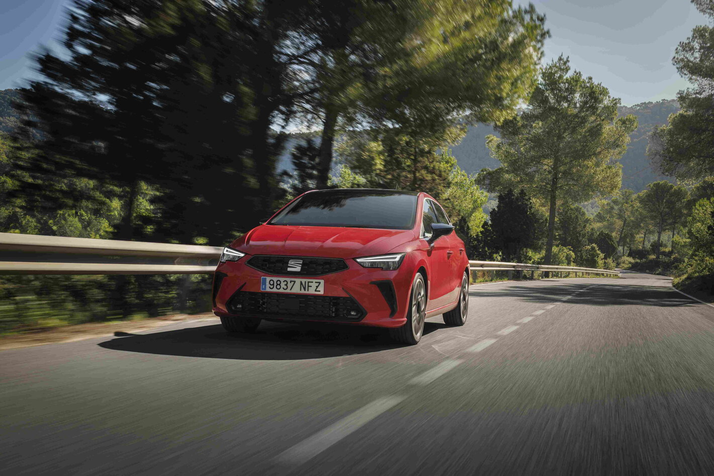 Rode Seat Ibiza, met dynamische velgen, rijdt op een kronkelende bosrijke weg.