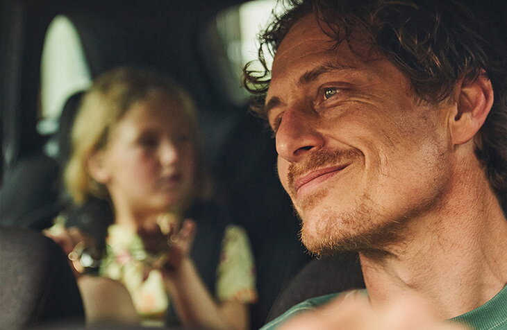 Vader glimlacht terwijl hij rijdt in een Škoda Fabia, met zijn kind spelend op de achterbank.