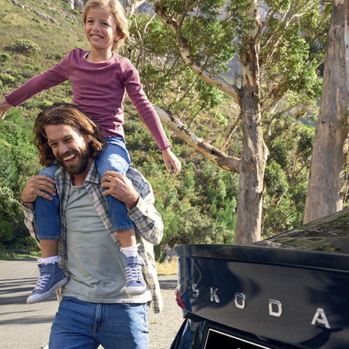 Vader draagt zijn kind op de schouders naast een Škoda Octavia in een groen berglandschap.