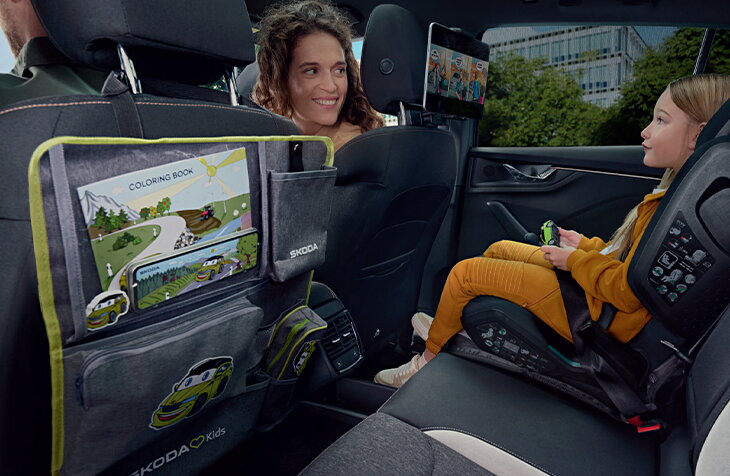Kind zit in een kinderzitje op de achterbank van een Škoda Scala, met Skoda Kids accessoires en entertainment aan de voorstoelen.