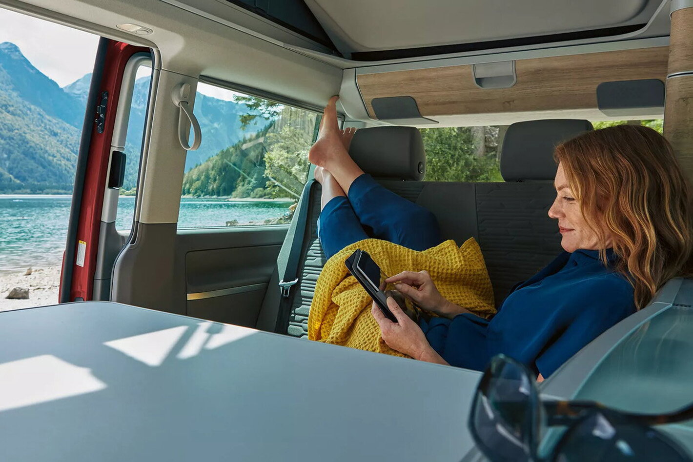 Volkswagen california vrouw ligt op achterbank aan een meer in de bergen