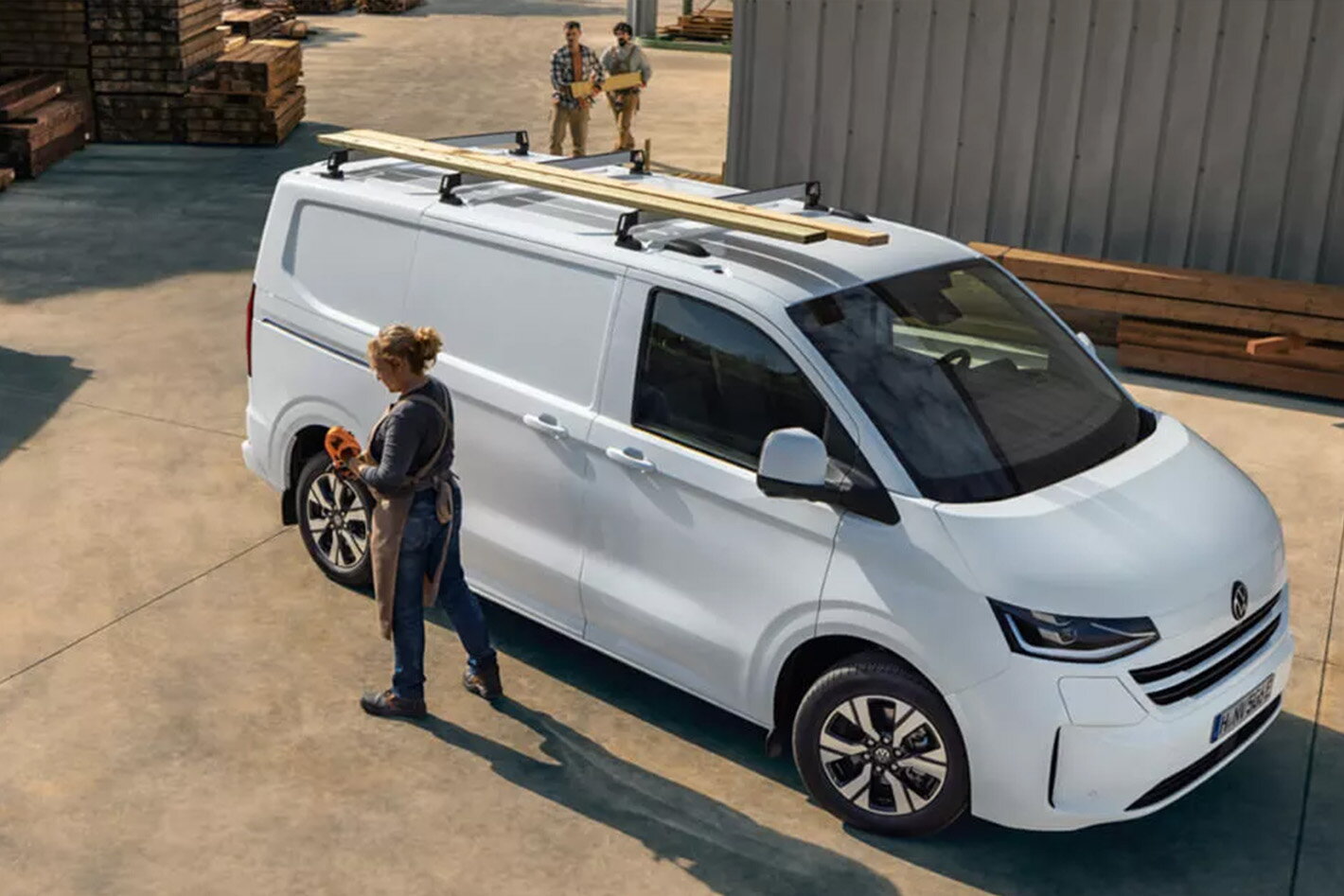 Volkswagen Transporter met vrouw en hout op dakrail op werf