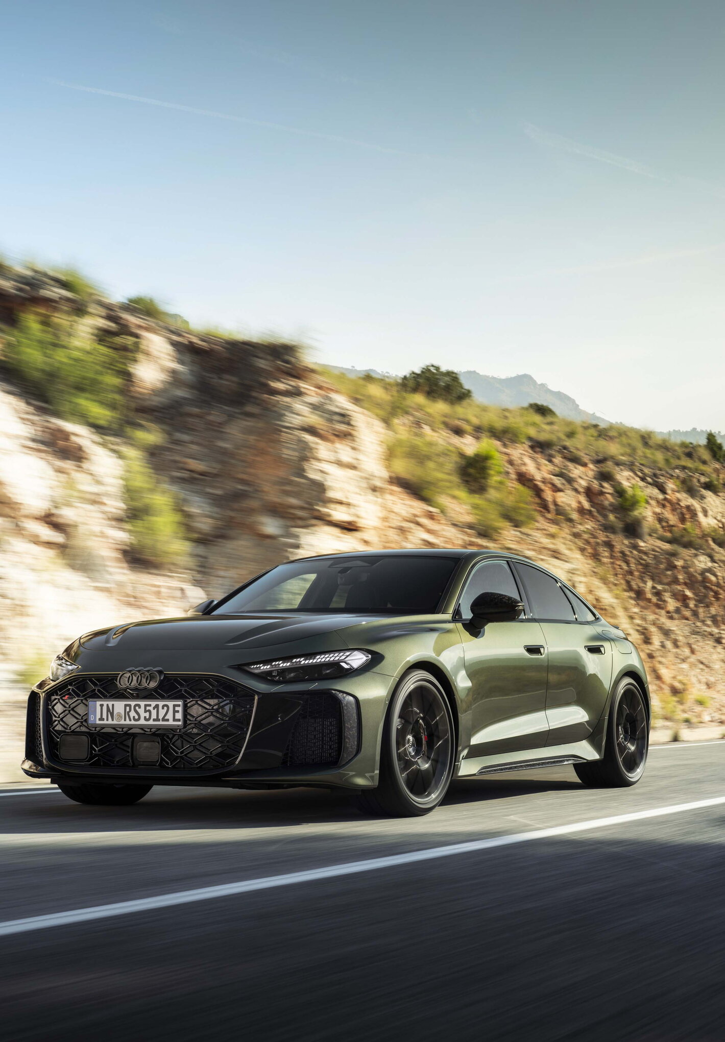 Vooraanzicht groene Audi RS5 die dynamisch over een bergweg rijdt onder een stralende zon