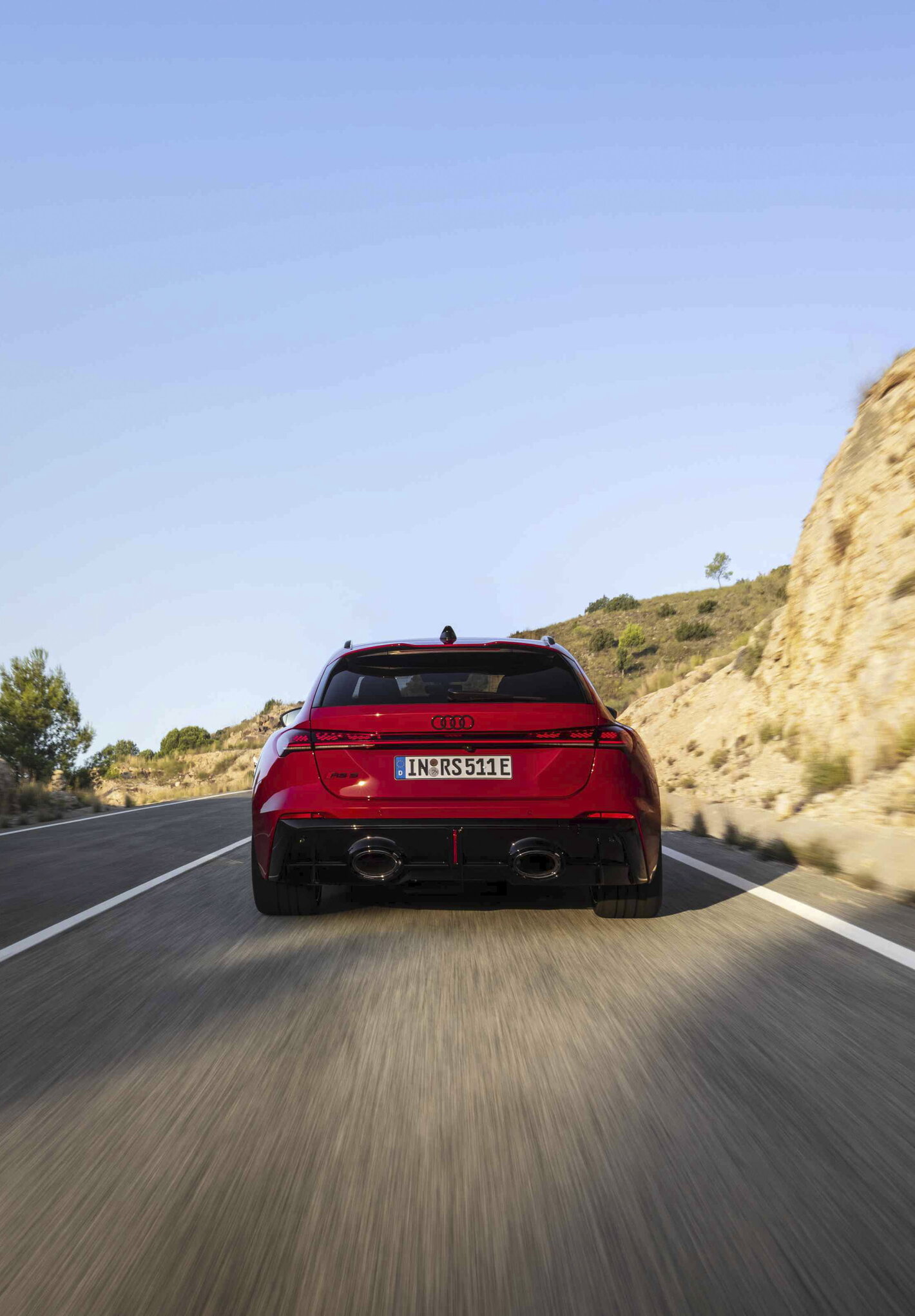 Rode Audi RS5 sportwagen rijdt over een bochtige bergweg bij zonsondergang.