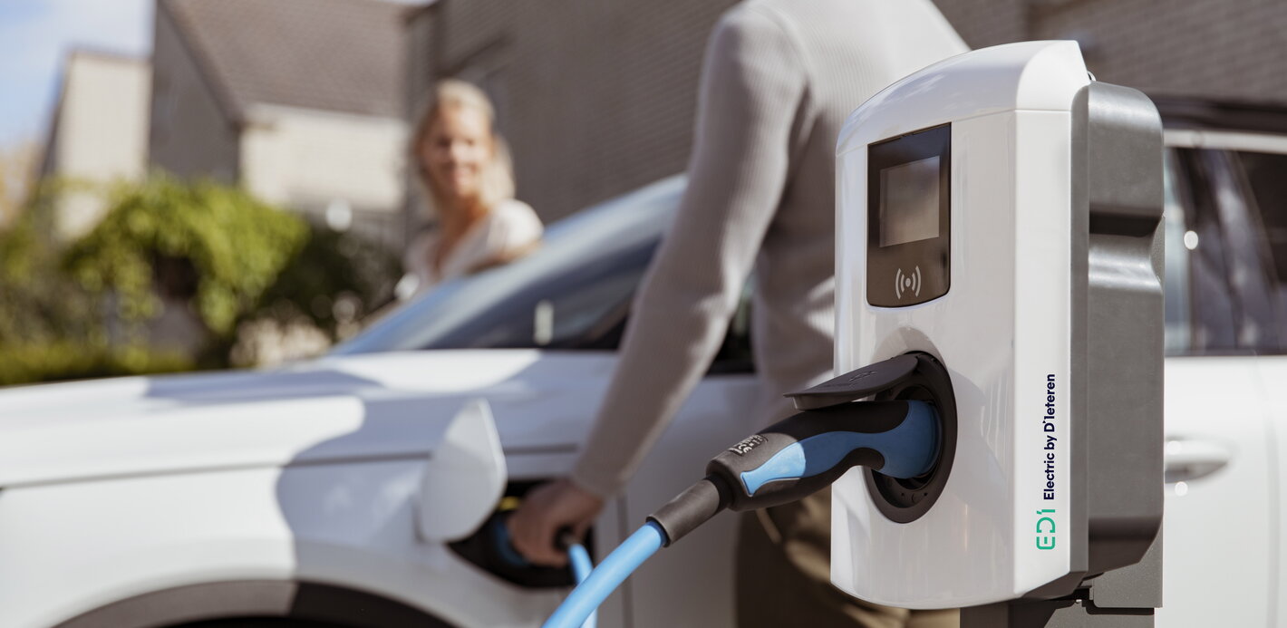 Een koppel staat op het punt om in hun elektrische wagen in te stappen die aan het laden is via hun laadpaal