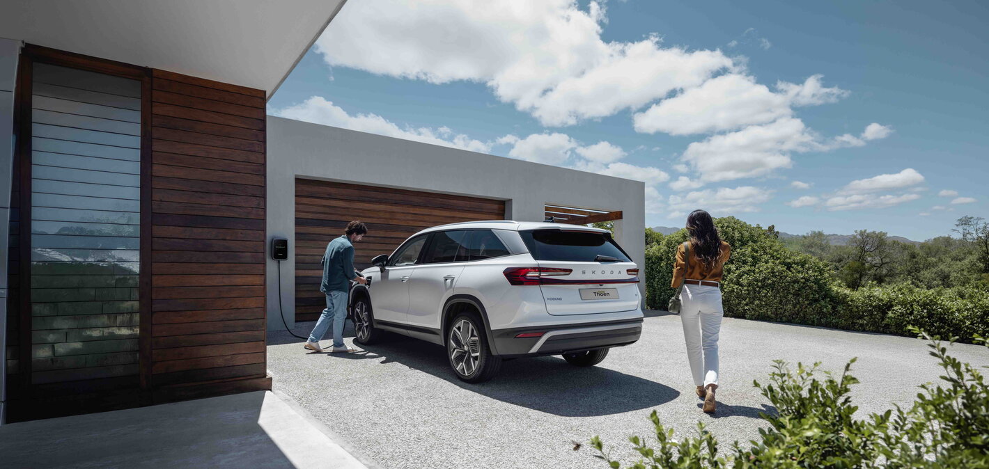 Een witte Skoda Kodiaq is thuis aan het laden met een koppel die op het punt staat in te stappen