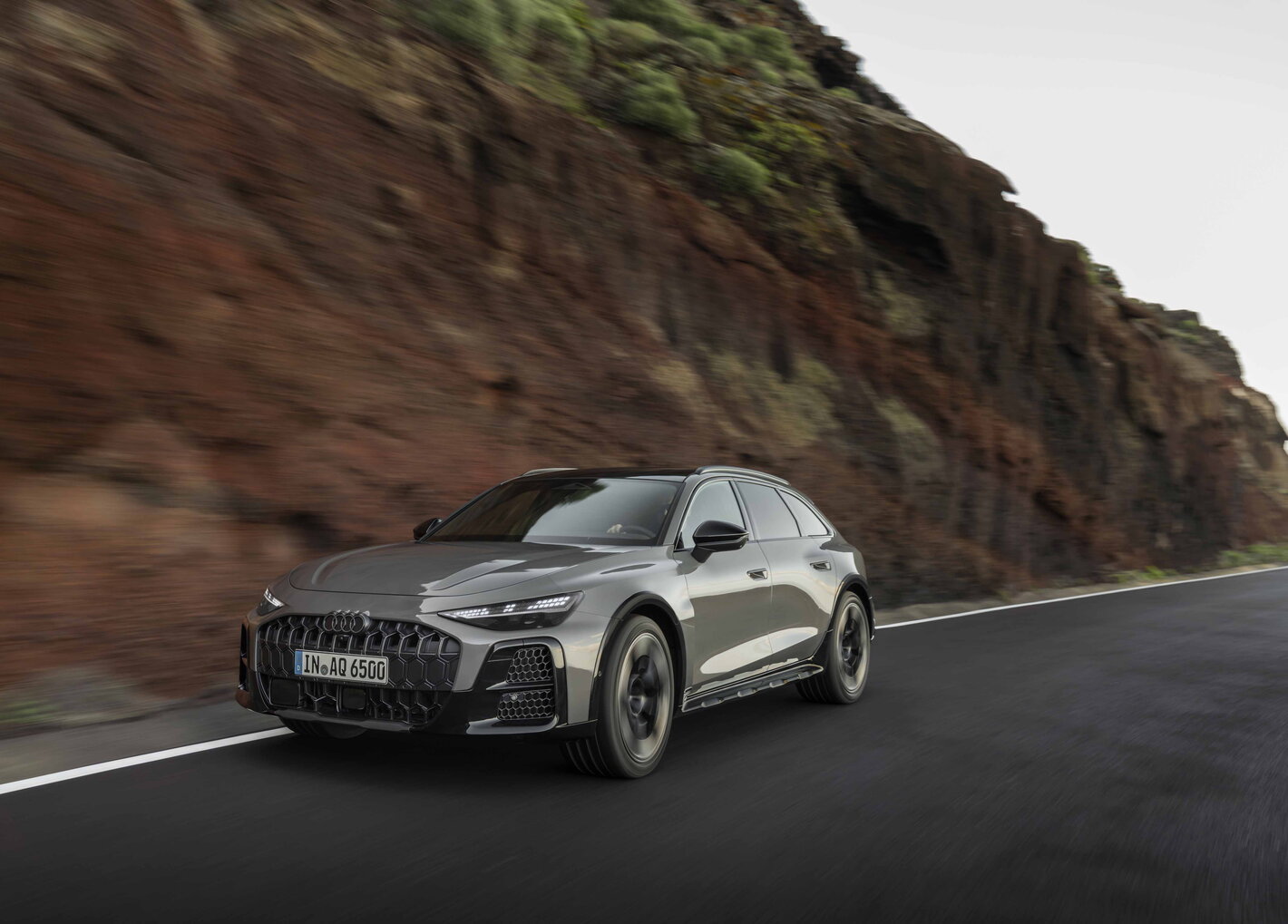 Grijze Audi A6 Allroad sportief rijdend op bochtige weg langs rotsachtige kliffen.